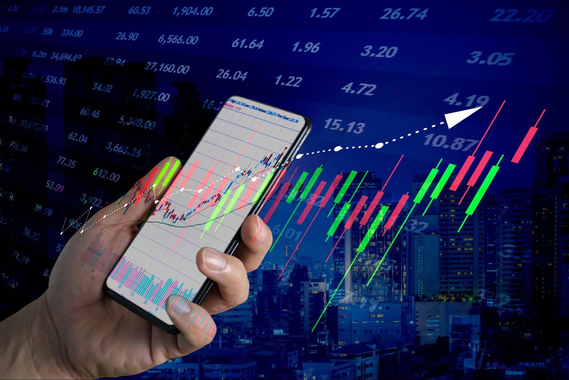 A hand holding a phone with a trading candlestick chart and other financial data like forex trading costs overlaid on top.
